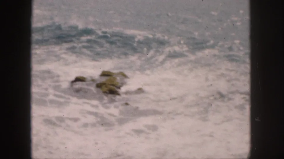 1959 Hawaii home-movie frame of rough surf breaking around low rocks near the shore.