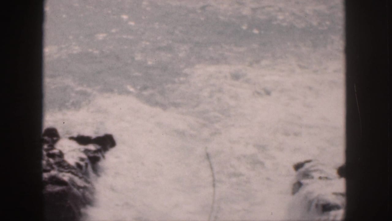 White surf breaks against dark rocks, framed by black film edges.