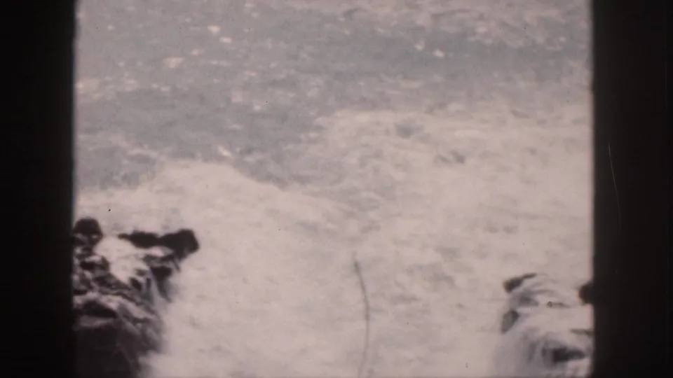 1959 Hawaii 8mm frame showing foamy surf striking dark shoreline rocks within visible film borders.