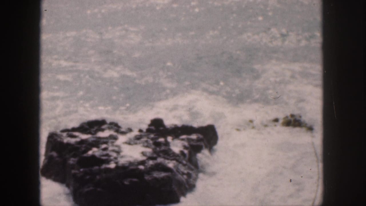 Foamy water surrounds dark rocks near the shore.