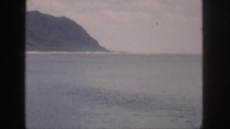 1959 Hawaii 8mm frame with a distant mountainous coastline beyond muted ocean water.