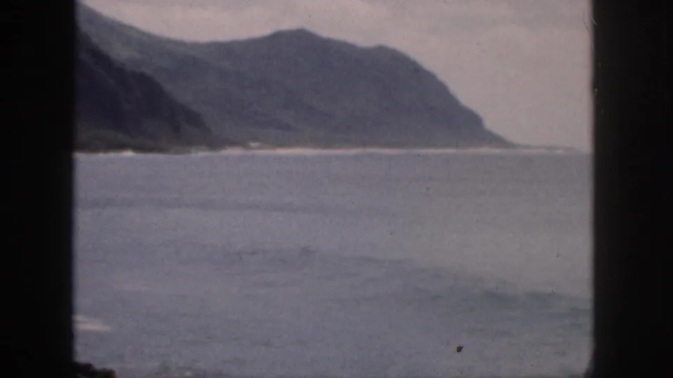 A distant Hawaii coastline and mountain slope appear across open water in a faded 1959 8mm frame.