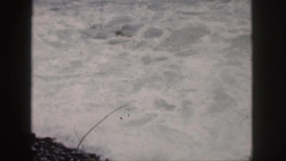 1959 Hawaii home-movie frame of rough ocean foam divided by a dark vertical camera or aperture edge.