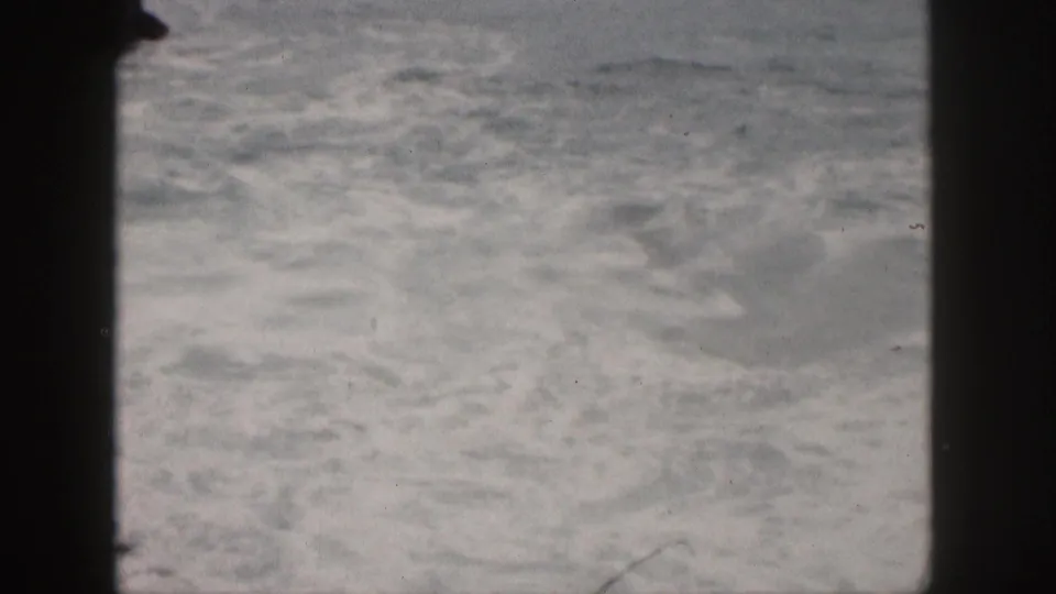 Faded 8mm Hawaii shoreline view with pale foam, ocean wash, and dark frame edges from the home-movie scan.