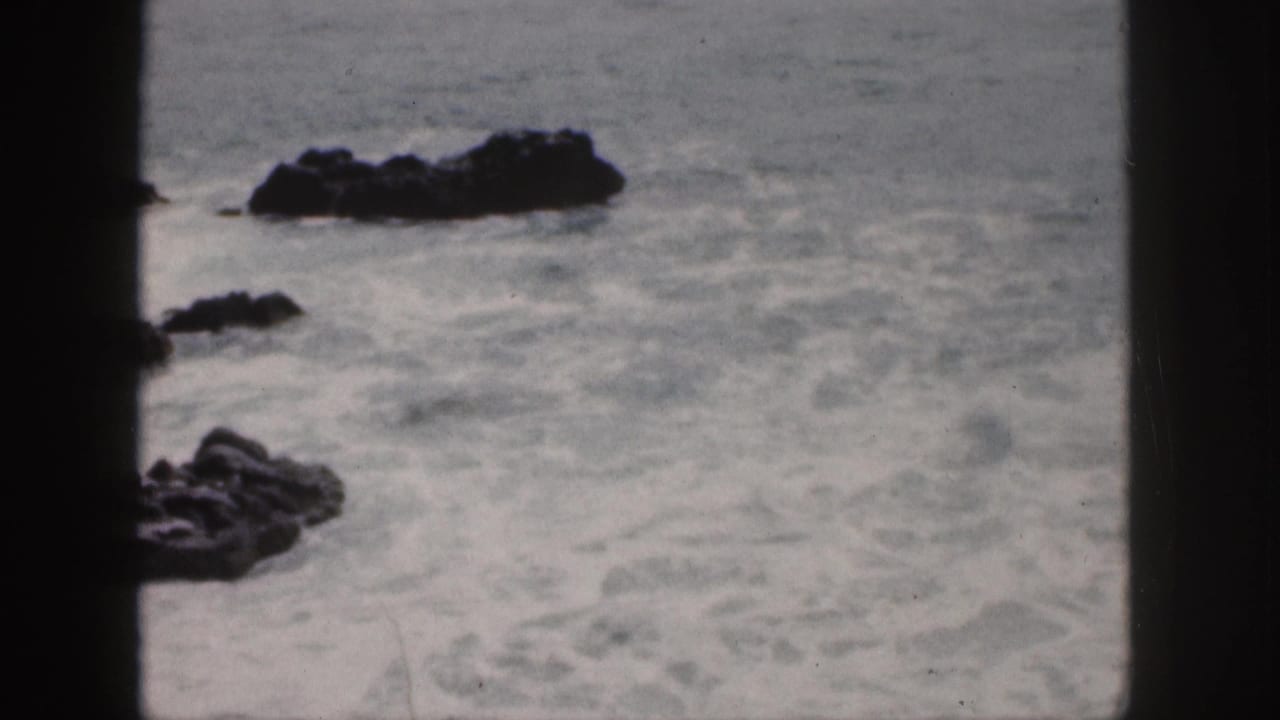 1959 Hawaii 8mm frame of foamy surf around dark coastal rocks, with soft focus and heavy film gate borders.