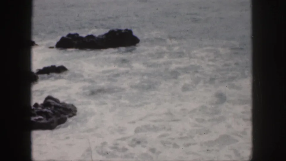 1959 Hawaii 8mm frame of foamy surf around dark coastal rocks, with soft focus and heavy film gate borders.