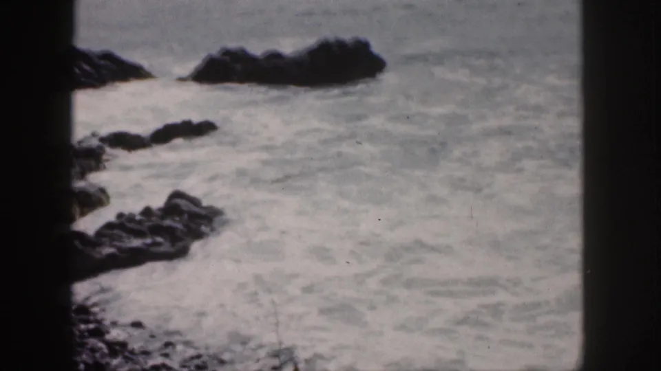 1959 Hawaii coastal frame with pale turbulent water, dark rocks, and visible 8mm frame borders.