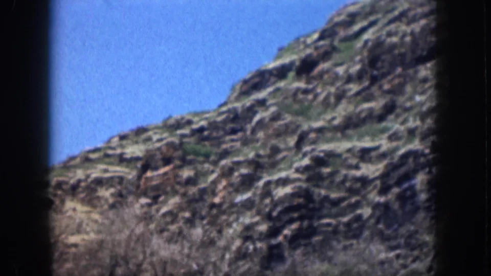 1959 Hawaii home-movie frame showing a slanting rocky hillside with brush at the base and clear sky.