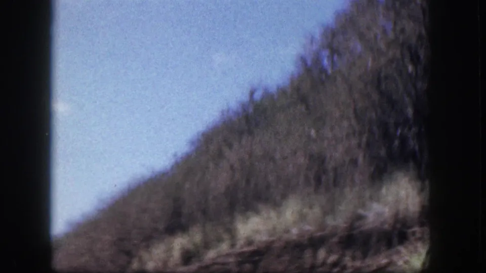 1959 Hawaii 8mm frame showing a soft-focus mountainside with dry vegetation, trees, and a small cloud.