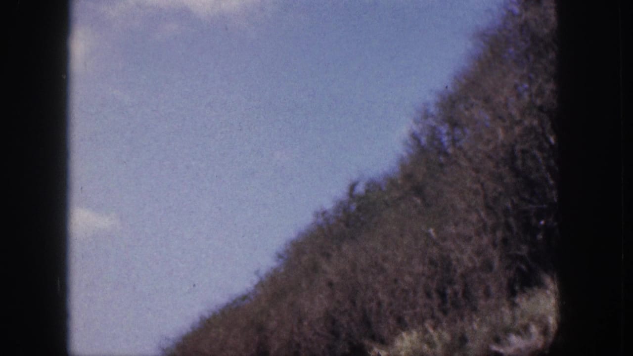 Rocky hillside rising against a pale sky, partly obscured by dark film-frame edges.