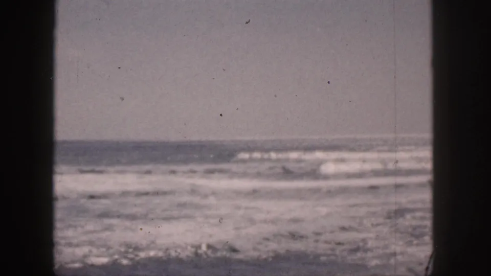 1959 Hawaii home-movie frame with turbulent surf, whitecaps, and a low ocean horizon split by dark vertical window framing.