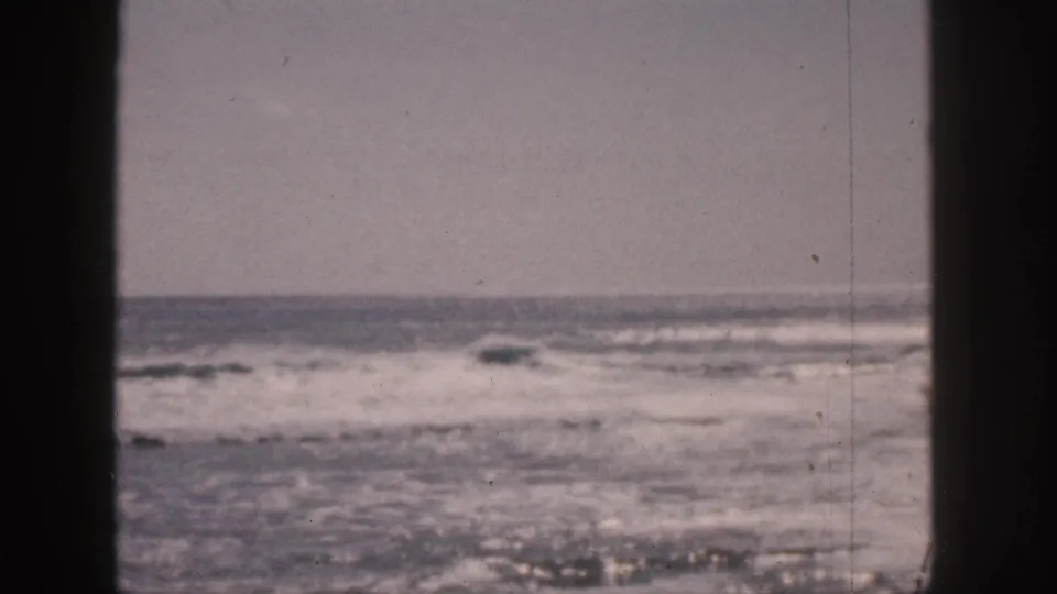 1959 Hawaii 8mm frame with rough ocean, whitecaps, gray sky, and dark vertical framing from a window or similar opening.