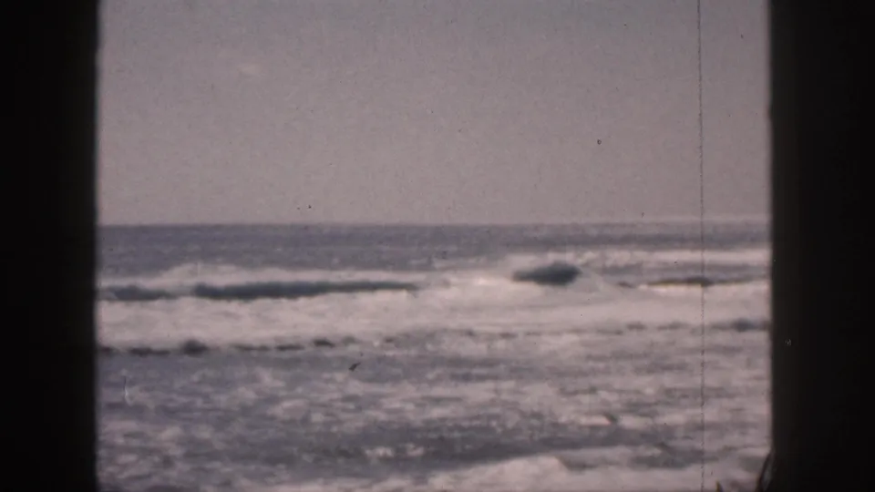 1959 Hawaii 8mm frame showing ocean surf, white foam, pale sky, and dark vertical edges suggesting a window or doorway view.