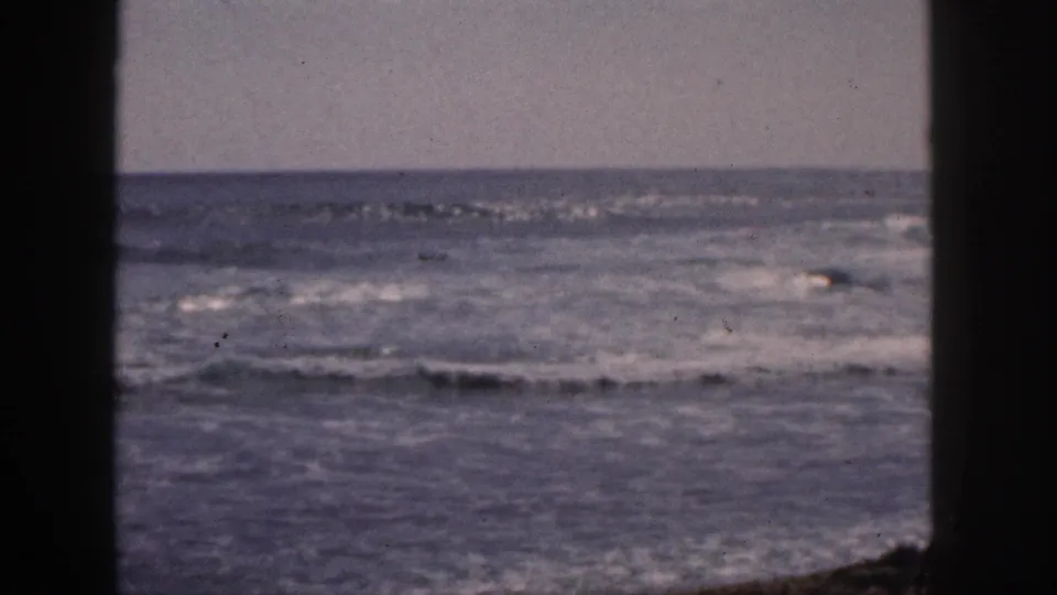 1959 Hawaii 8mm frame of foamy ocean waves under a pale sky, bordered by dark vertical edges and visible film wear.