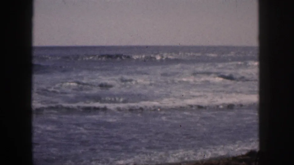 1959 Hawaii 8mm frame showing rolling surf and a level horizon viewed through dark vertical foreground framing.