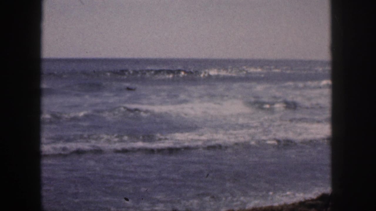 1959 Hawaii home-movie still with choppy surf, pale sky, and dark foreground edges suggesting a shaded opening.