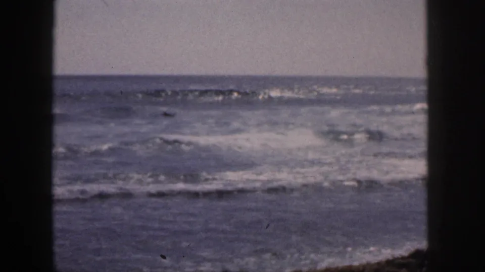 1959 Hawaii home-movie still with choppy surf, pale sky, and dark foreground edges suggesting a shaded opening.