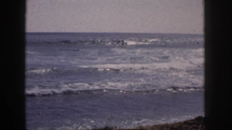 1959 Hawaii 8mm frame showing foamy shoreline surf and open ocean, with dark vertical foreground framing.