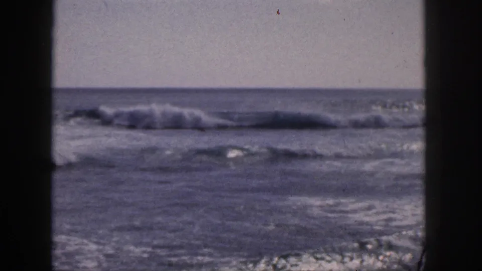 1959 Hawaii home-movie still showing a low breaking wave and blue-gray water framed by dark foreground edges.