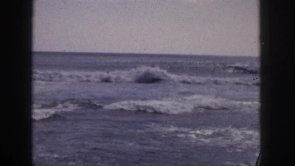 Faded 1959 Hawaii 8mm coastal frame with foamy waves, open water, and dark film edges.
