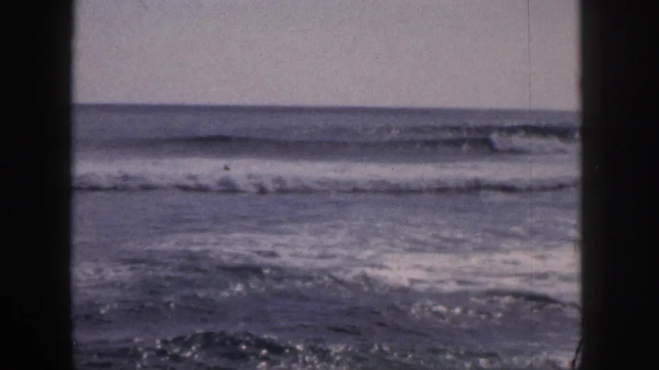 1959 Hawaii 8mm still showing foamy shoreline water viewed through dark foreground framing.