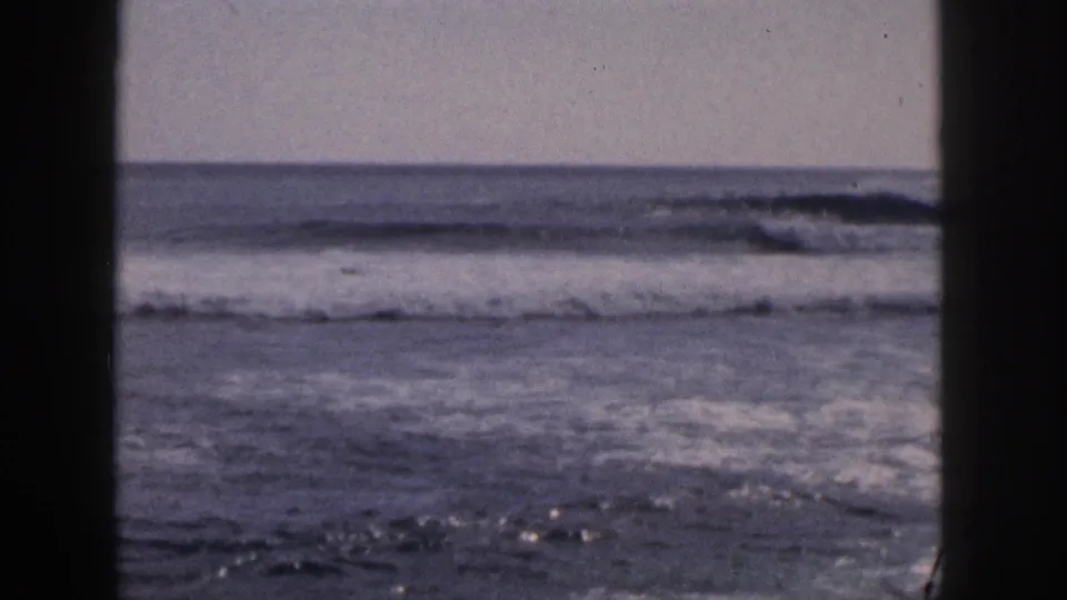 1959 Hawaii home-movie frame of surf and white foam seen past dark window or doorway framing.