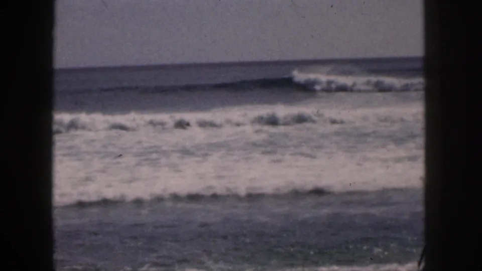 1959 Hawaii home-movie frame of foamy nearshore water and rolling surf through dark vertical framing.
