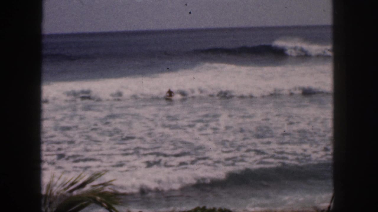 Surfer in shallow breaking waves with ocean swell beyond dark foreground bars.