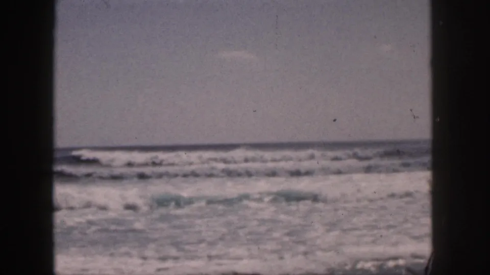 1959 Hawaii 8mm frame of rolling ocean surf seen through dark vertical edges, with no landmark visible.