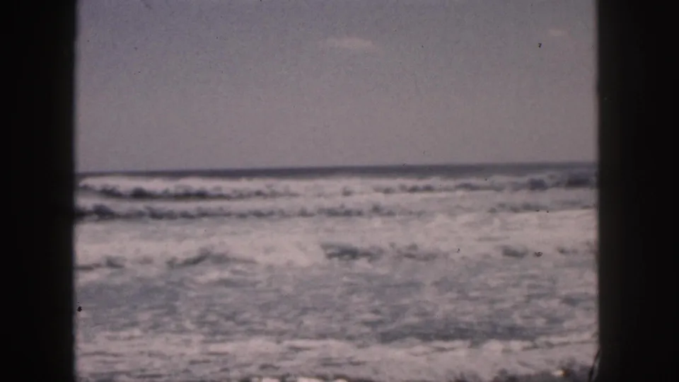 1959 Hawaii 8mm frame showing foamy ocean surf and horizon, with dark foreground framing from the filming position.