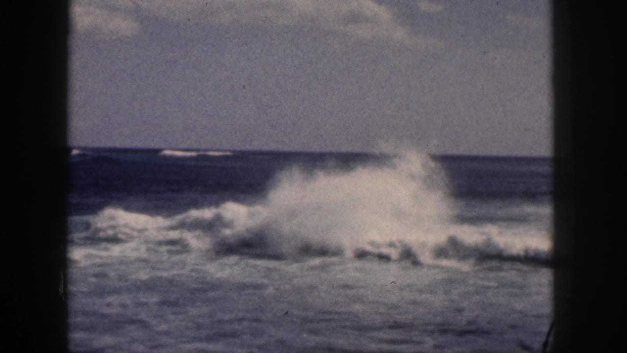 1959 Hawaii 8mm frame showing a burst of white surf spray over dark blue water beneath a hazy sky.