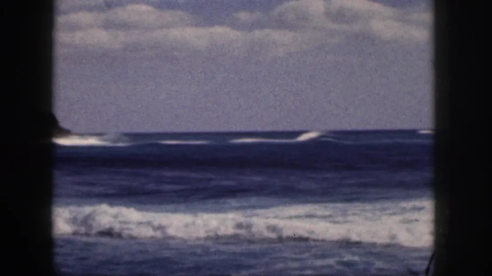 1959 Hawaii coastal view with white surf lines beyond a dark central post and soft, grainy sky.