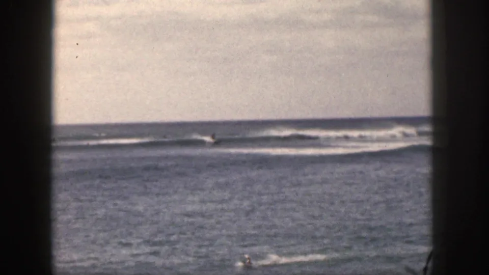 1959 Hawaii 8mm frame showing open water, low surf lines, cloudy sky, and a small person in the water near the lower right.