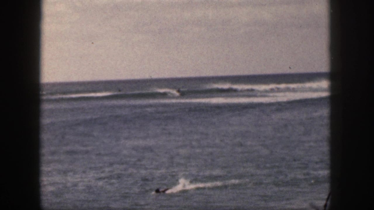 Distant swimmers or paddlers in ocean water with breaking waves beyond a dark film-frame border.