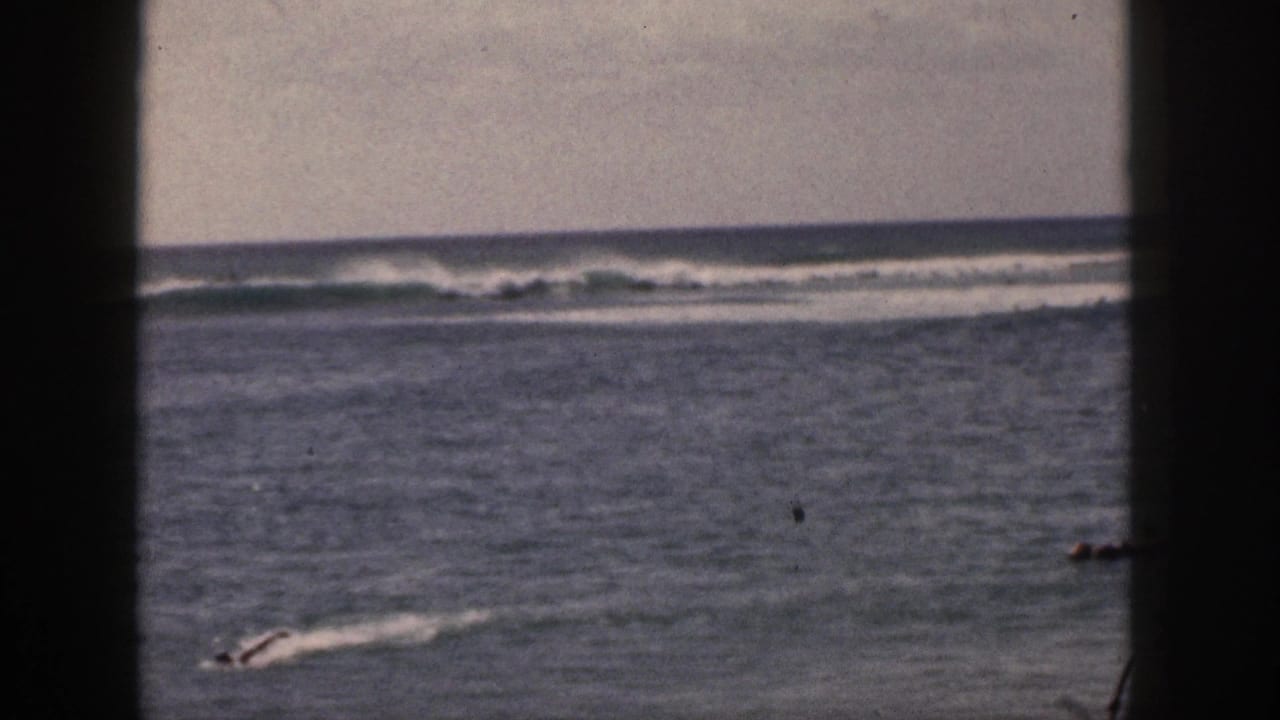 One distant person appears to paddle across calm ocean water with surf breaking in the background.