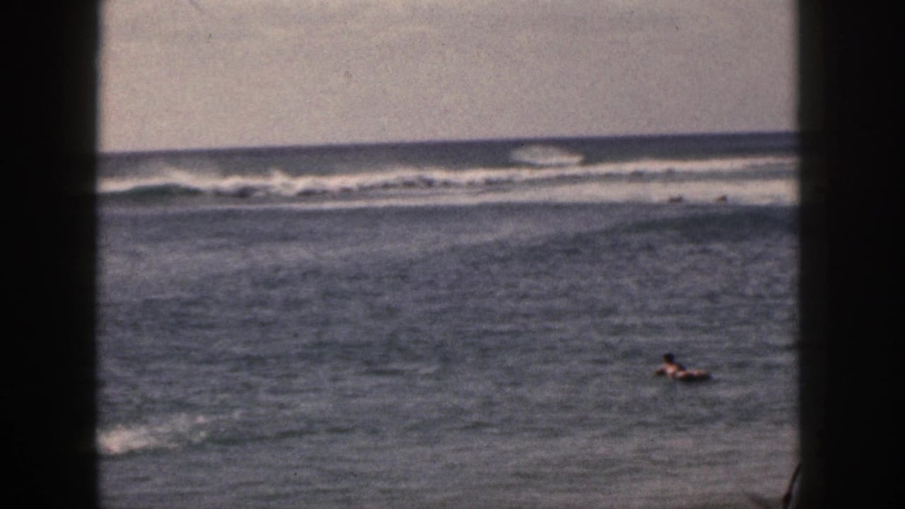 1959 Hawaii 8mm view of a distant person in the ocean, rolling waves, shoreline foam, muted color, and a dark film-frame divider.