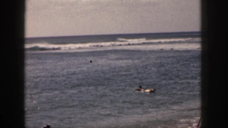 1959 Hawaii ocean frame with distant figures or a board rider at lower right, open water, offshore surf, pale sky, and 8mm grain.