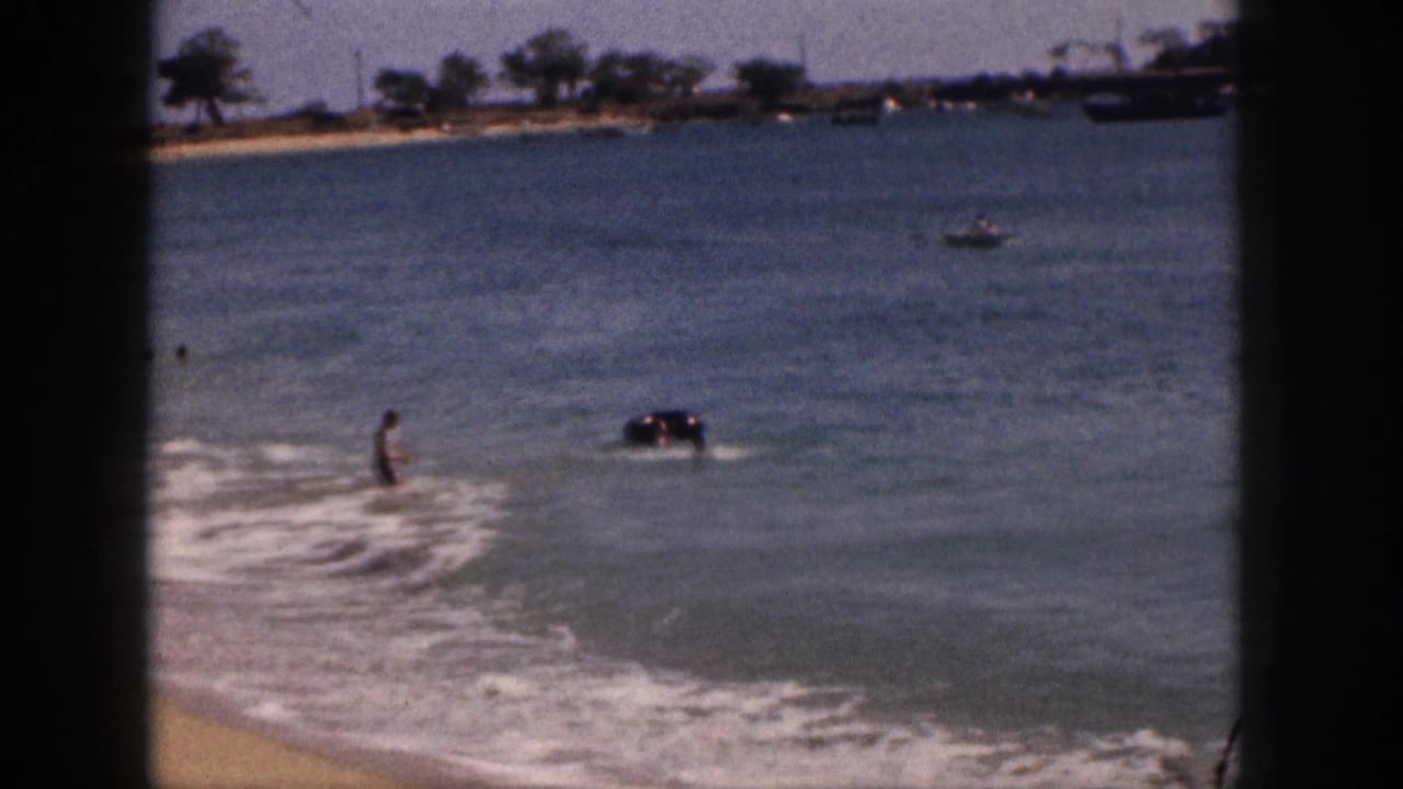 Person wading near breaking waves with an inner tube floating farther out.