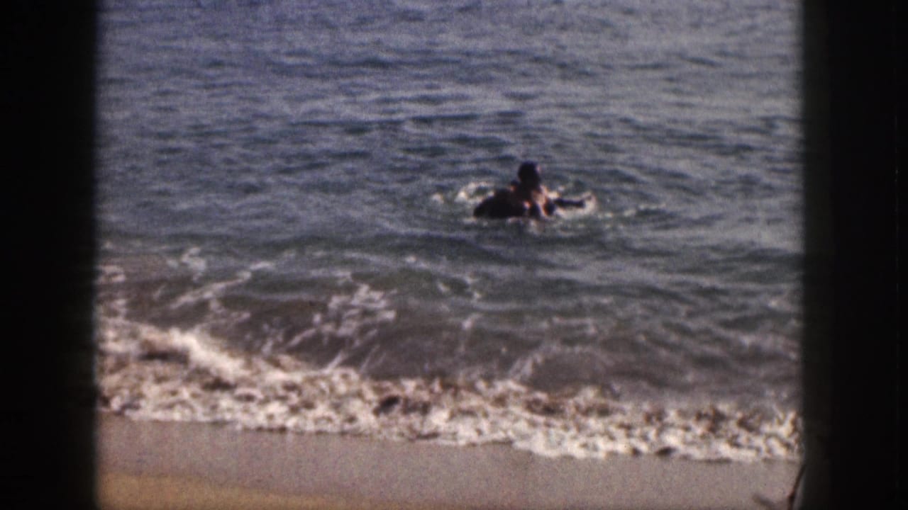 A swimmer holds or floats near an inner tube in choppy ocean water.