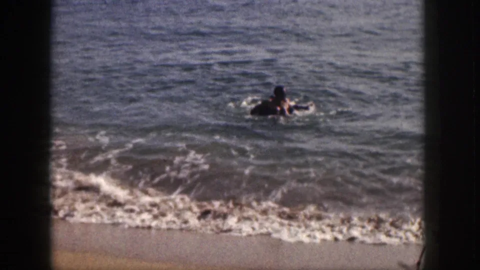 A person floats or plays with an inner tube in the ocean during a 1959 Hawaii beach scene.