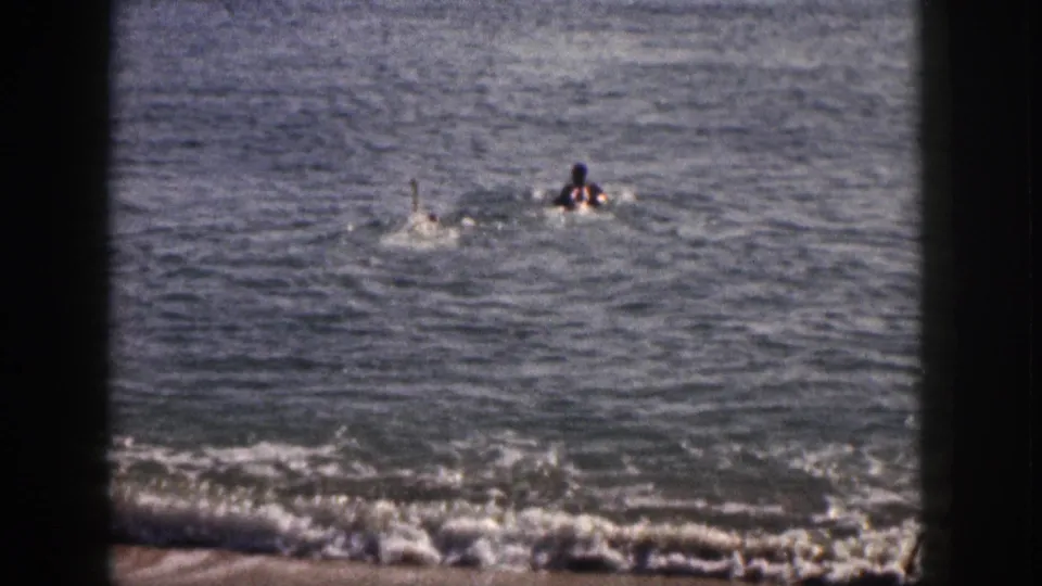 Two swimmers splash offshore in grainy 8mm footage from a Hawaii beach in 1959.