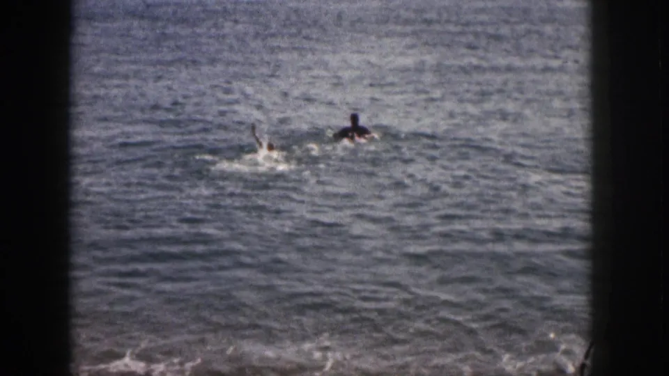 Two distant figures swim and splash in open water in a brief 1959 Hawaii beach home movie shot.