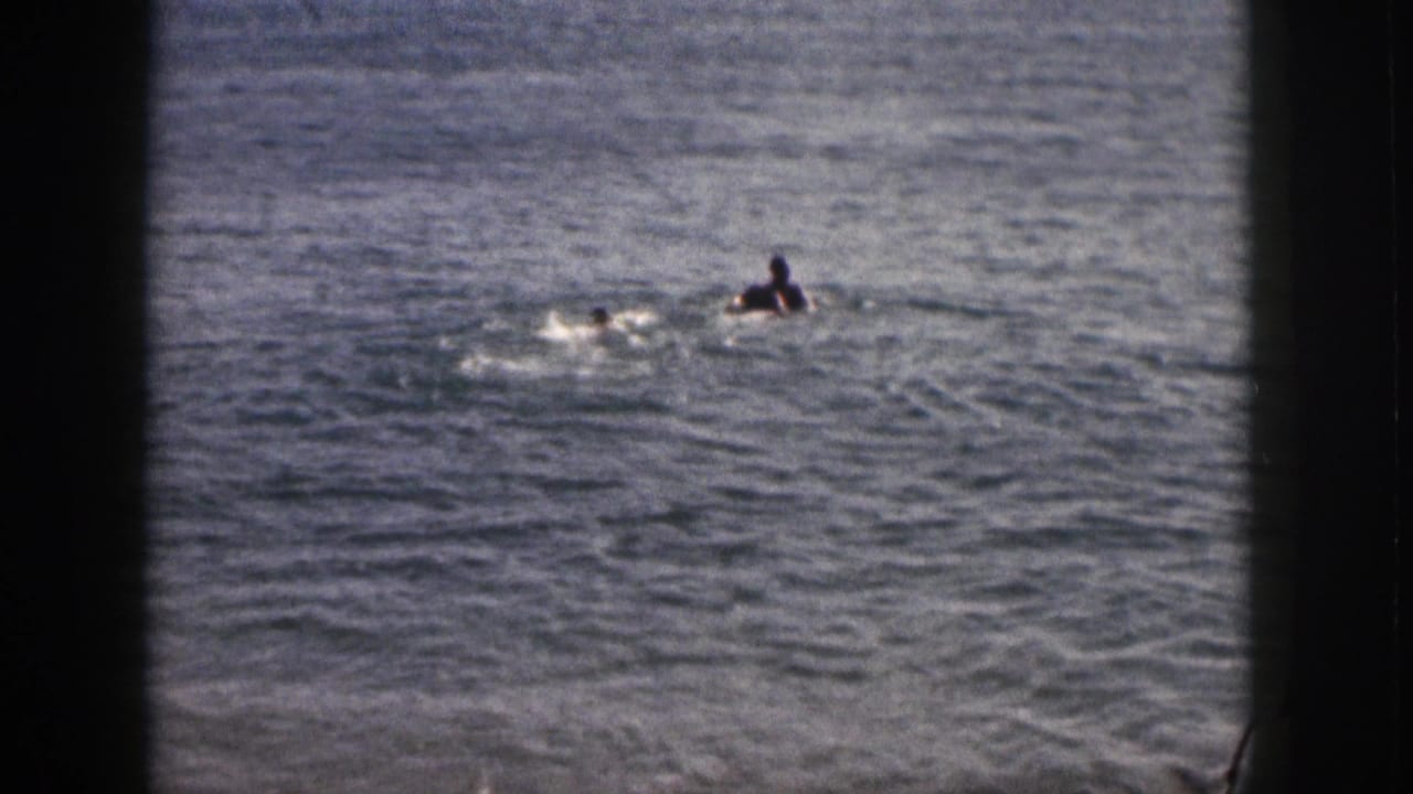 Two people swim in ocean water seen through dark window-frame edges.