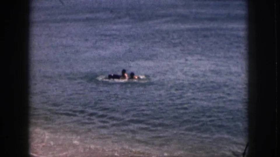 Two swimmers are visible near the surface of Hawaii coastal water in a soft, faded 8mm frame.