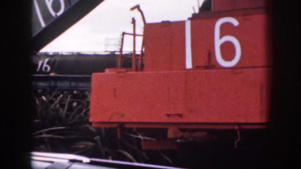 Close 1959 Hawaii home-movie view of red agricultural machinery marked 16, with dark metal equipment behind it.