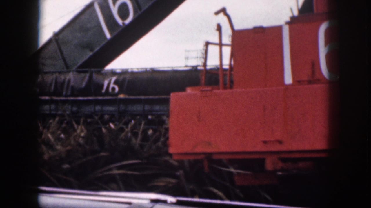 1959 Hawaii 8mm frame showing red industrial equipment and a dark structure marked 16, viewed from inside a vehicle.