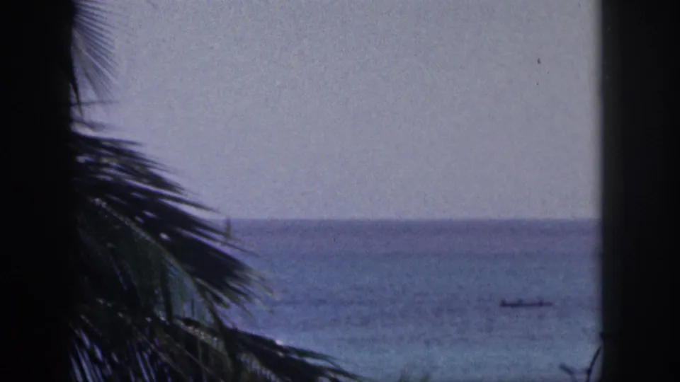 1959 Hawaii 8mm frame with dark palm shapes in the foreground and a small distant boat on blue water.
