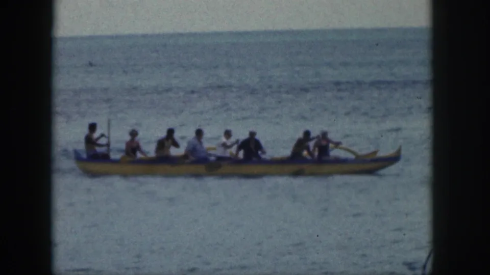 The outrigger canoe continues across Hawaiian open water with paddlers seated in a line and stroking together.