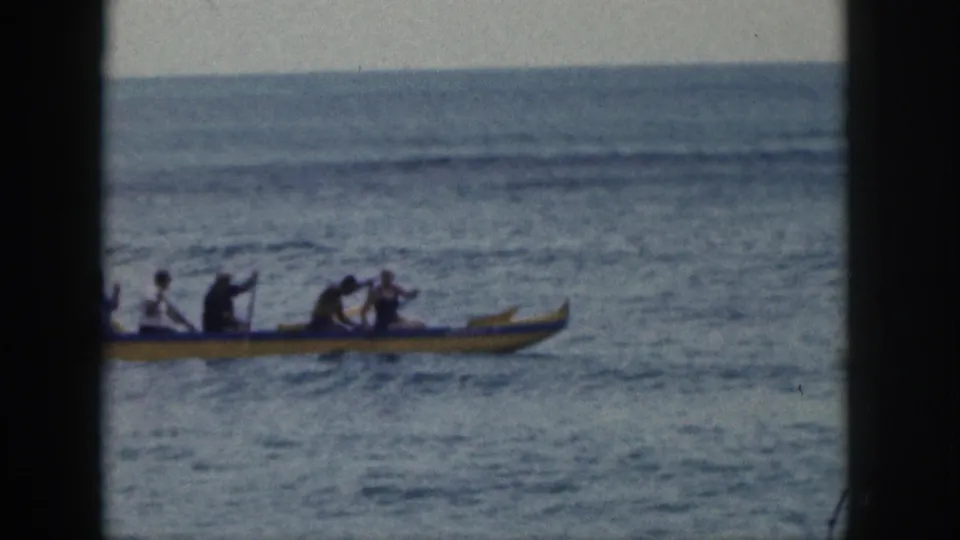 The canoe nears the right side of the frame as paddlers continue across open water in the 1959 Hawaii footage.