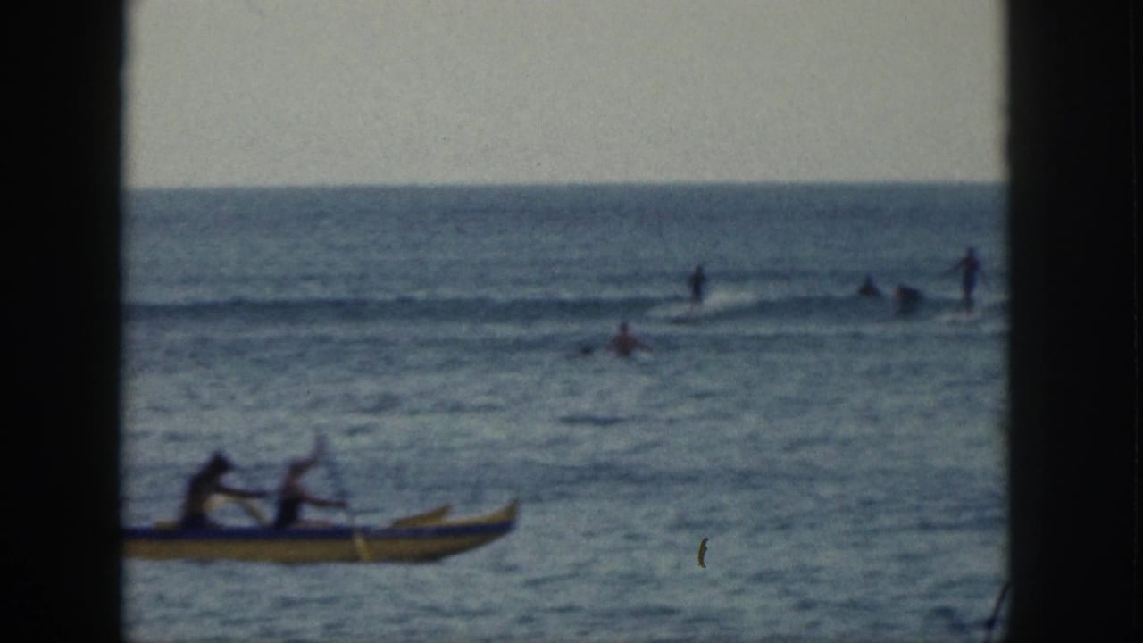 A yellow outrigger canoe passes in front of distant people in the surf.